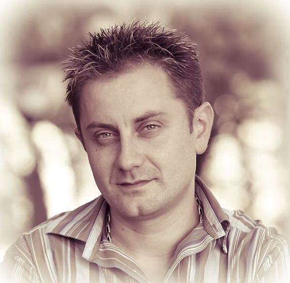 A person with short, spiky hair and a striped shirt looks at the camera, with a blurred, neutral background behind.